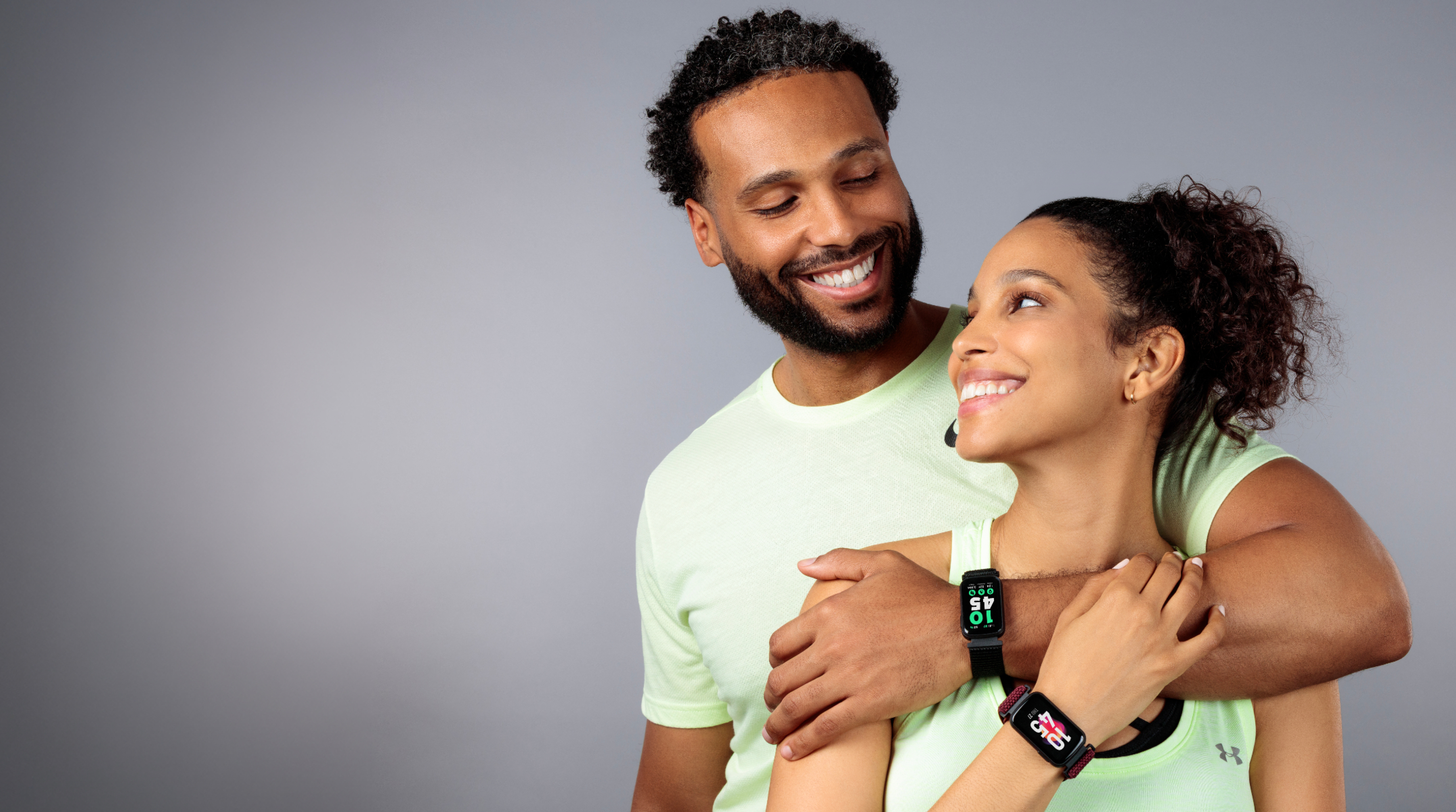 Two people wearing green shirts and smartwatches on a gray background
